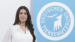 Porträt von Derya Özdemir, die vor dem Logo des Deutschen Tierschutzbundes steht