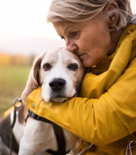 Traurige, ältere Frau mit Hund im Arm bei herbstlichem Wetter