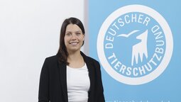 Portrait of Laura Ackermann standing in front of the logo of the German Animal Welfare Federation.